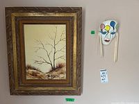 Framed painting and ceramic mask displayed on a wall with tags.