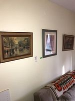 Three framed prints hanging on a wall above a couch, showing city street scenes including horse-drawn carriages and pedestrians.