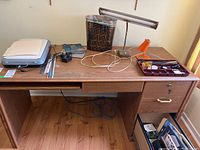Desk setup showing HP Scanjet G3010 scanner with cables, two table lamps, brown trashcan, assorted office supplies, and a wooden desk with storage drawers, hardwood floor visible.