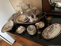 Wide view showing various silver plated items including the large tray, goblets, small bowls, spoons, and serving dishes arranged on a dark surface.