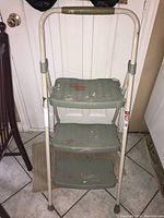Front side view of three-step metal step stool with paint stains.