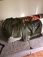 Olive green leather jacket and matching skirt displayed on a couch, showing front view and material texture.