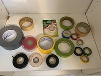 Photo showing various rolls of tape in multiple colors including gray duct tape, beige masking tape, green, blue, red, yellow colored tape, and black electrical tape.