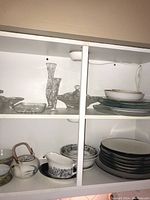 Two shelving units containing various glass vases, bowls, plates, and ceramic serveware including a tall textured clear glass vase and a stack of ceramic dishes.
