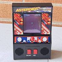 Front view of the vintage ASTEROIDS handheld mini arcade game powered on showing the game screen and controls.