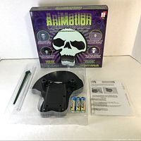 Front view of the box along with the base for the skull, pole, three batteries, and instruction manual inside plastic packaging.