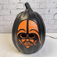 Black pumpkin with carved Darth Vader face design shown unlit.