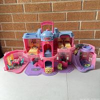 Fisher Price Sweet Streets Hotel unfolded showing multiple rooms including bedroom, dining area, and bathroom with furniture and accessories inside, all in pink and purple plastic.