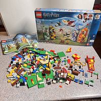Set components including colorful Lego bricks, mini-figures, broomsticks, Quidditch goalposts, and accessories spread out in front of the original box and instruction manuals.