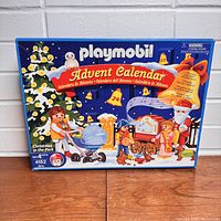 Front image of Playmobil advent calendar box for Christmas in the Park 4152 set, showing colorful illustration of winter park with Santa and children.