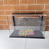 Front view of the toy display case showing the clear plastic enclosure with black and white check fabric interior and colorful paper inside.