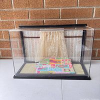 Front view of acrylic and wood toy display case showing fabric background with lace curtain and fabric floor.