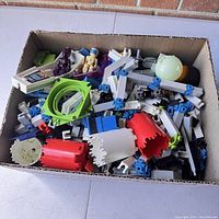 Box full of assorted vintage Fisher Price Construx toy building parts, figures, and connector pieces.