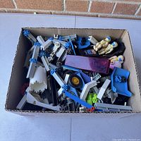 Box containing assorted plastic components of Fisher Price Construx toy set including beams, connectors, wheels, and robot pilot figures.