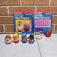 Vintage Fisher Price Little People Mini-Popper and Mini-Vacuum sets in original packaging with four plastic figurines placed in front.