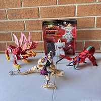 Complete lot showing four robot and dinosaur robot toys on table in front of brick wall.