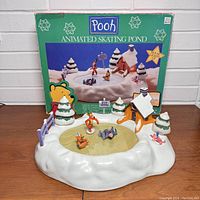 Winnie the Pooh Animated Skating Pond with original box behind, showing figurines skating on pond and snow-covered trees and cabin