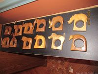 Top-down photo showing all 12 wooden animal-shaped napkin ring holders arranged in two rows on a black surface.