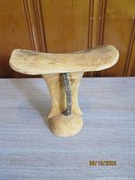 Front view of the antique wooden African headrest showing the gently curved top surface, vertical central support, and the rounded base with cord detail.