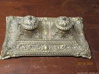 Top angled view of the ornate brass double inkwell showing embossed decorative details and closed hinged lids.