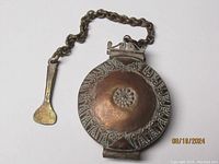 Top view of round snuff box showing domed lid with embossed floral center and patterned border, attached chain and small spoon visible.