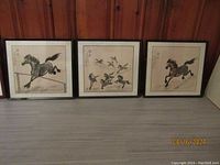 Three framed Chinese ink on paper paintings displayed side by side on floor against wall, two of horses and one of flying birds.
