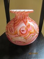 Side view of coral colored mouth-blown glass vase showing swirls of coral, orange, pink and white