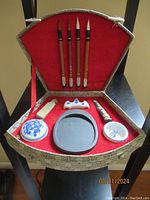 Full view of vintage Chinese calligraphy set in original red velvet-lined, ornate fabric case showing brushes, ink stick, brush holder, porcelain dishes, red ink container, and chop.