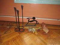 Full view of lot with all four items on wood floor against orange wall: leather corded ceramic vase, copper object, black animal sculpture and tall black candleholder.