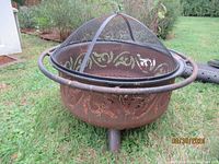 Metal wood burning fire pit with decorative scroll cutouts and dome mesh cover with top handle.