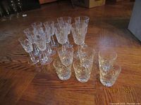 Photo showing a group of Galway Crystal glasses arranged on wooden floor, including tall stemmed and lowball glasses with detailed Clifden pattern etching.