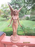Front view of the 15 inch tall iron angel statue figurine with wings and flowing gown, standing on circular base outdoors.