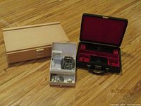 Three jewelry boxes on wooden floor: large wooden box, black leather-like jewelry case open showing red velvet interior, white tray with various pieces of costume jewelry
