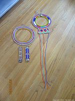 Photo showing multiple pieces, including two circular necklaces with colorful beadwork and a pair of matching earrings on a hardwood floor.