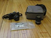 Top view of Nikon FM camera, Tiffen 52mm lens, and original camera case laid out on wood floor