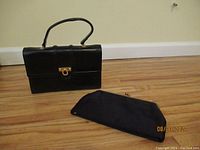 Black leather handbag from Greece alongside a black formal clutch bag on hardwood floor