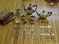 Overview photo showing tea pot, coffee pot, creamer, sugar bowl, condiment dishes, cutlery, salt and pepper shakers, and tarnish bags.