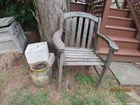 Teak chair and stone planter shown outdoors next to steps, on grass with trees nearby