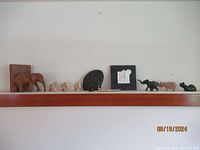 Photo showing the entire collection of elephant figurines displayed on a shelf including the wood bookend, soapstone elephants, clay tile, stone carved figurines.