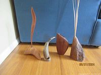 Four hand carved wood sculptures displayed side by side on wooden floor with blue couch background showing an overview of lot pieces.