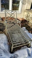 Full view of the metal chaise lounge outdoors, showing the slatted frame and X design on backrest.