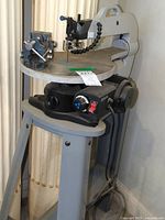 Three-quarter view of scroll saw on stand showing table, motor and bench vise clamp
