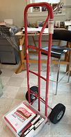 Front view of red metal dolly with wheels and box of sandpaper placed on its base.