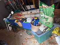 Garden cart loaded with bags of fertilizer, burlap rolls, tools, and watering can.