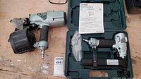 Coil nailer and power stapler side by side, stapler in open carrying case with manual