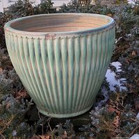 Overall view of one green glazed ceramic planter placed outside among shrubs, showing its large size and vertical ribbed design