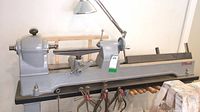 Full side view of lathe on stand showing bed, headstock, tool rest, chisels stored beneath.