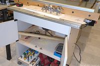 Front view of router table stand showing lower shelf with bits and router