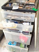 Full view of black-topped plastic storage organizer with 4 pull-out clear drawers containing various hardware items
