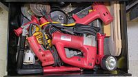 Drawer with Milwaukee red power tools: drill, jigsaw, cords, and accessories in mixed used condition